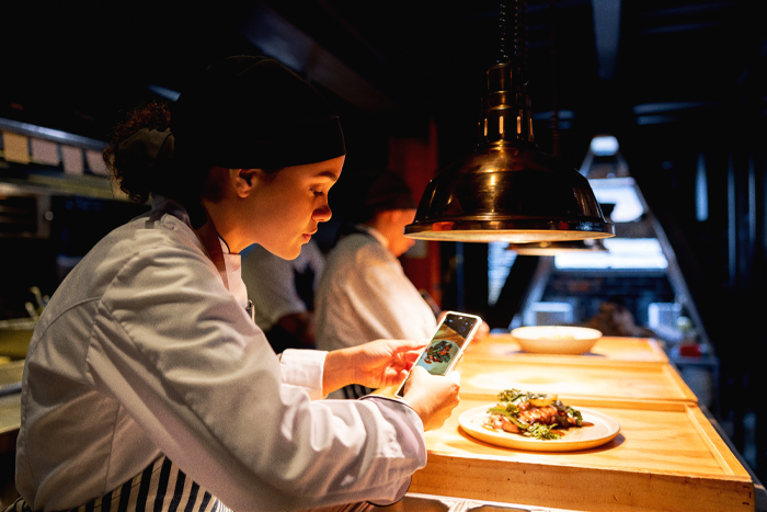 A chef taking a picture of a plate of food in a kitchen with a phone