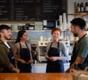 Four staff members having a team huddle behind the counter of a café, ready to start their summer shift.