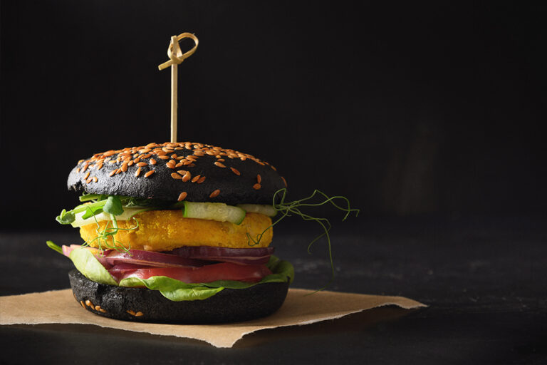 Vegan burger dressed with tomato and lettuce, in a charcoal bun.